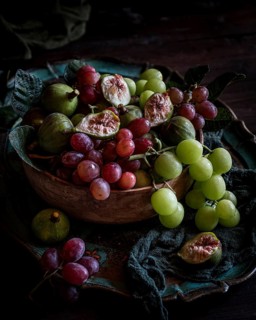 A rustic bowl filled with an assortment of fresh fruits, including green and red grapes alongside