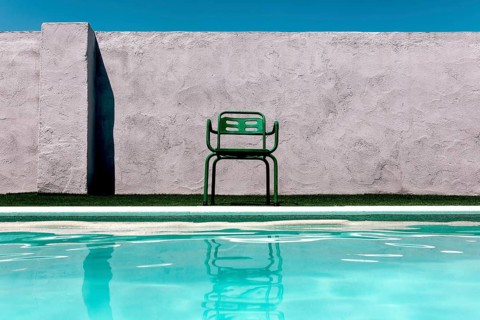 A vibrant green chair sits beside a serene pool, contrasting a textured concrete wall under a clear