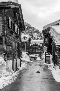 Street with historic old snow-covered wooden houses, black and white photo, mountain village Zinal,