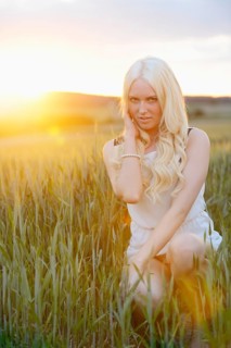 A blonde woman kneels in a grassy field at sunset, illuminated by warm sunlight