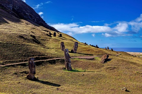 A hilly landscape with several Moai statues and sea views under a clear sky, The Moai Statues on