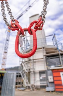 Large red hook with chain hangs in front of a blurred construction site background, staircase