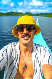 Young man wearing sunglasses and bucket hat taking selfie while enjoying boat trip in the beautiful