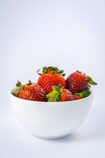 A white bowl with precious strawberries inside