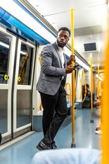 Young businessman holding handrail and using smartphone on subway train during his daily commute to