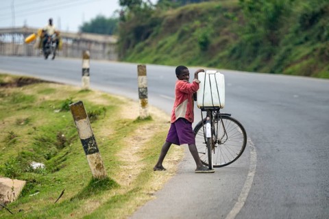 A boy transports water on a bicycle on a country road, street scene in rural Uganda, western