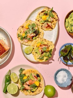 Top view of vibrant, colorful tacos arranged creatively on a pastel pink background. The