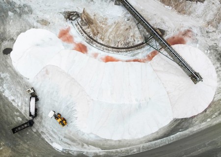Salt heaps with conveyor belt, lorry and excavator at the salt works of Walvis Bay Salt. Aerial