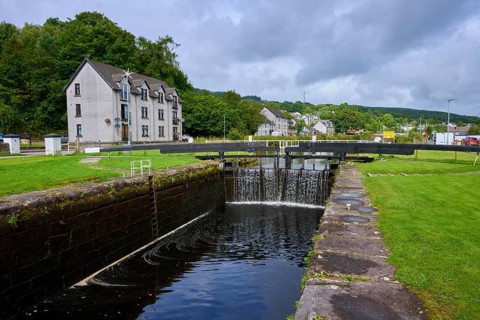 Lock with water and neighboring buildings nestled in a green, cloudy environment, Ardrishaig,