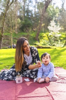 Happy mother feeding her baby solid food with a spoon while having a picnic lunch outdoors in a