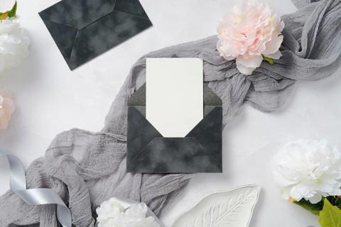 Elegant wedding stationery featuring dark envelopes and blank cards, styled with soft gray fabric