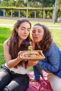 A romantic young women couple blows out a '5' candle on a cookie anniversary cake while sitting on