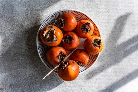 A close-up top view of freshly picked ripe persimmons neatly arranged on a stylish white and blue