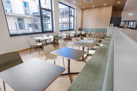 A simple and modern canteen with seats and large windows, which is decorated in a bright design and