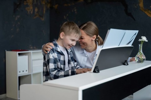 A joyful mother embraces her young son as they sit together at the piano, sharing a moment of