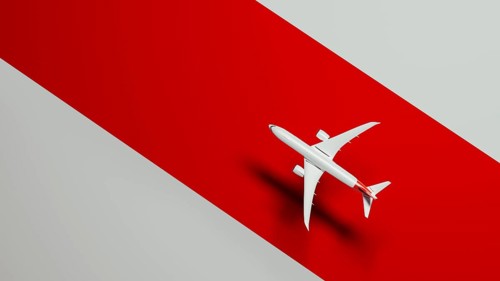 From above a sleek commercial airplane soars gracefully above a vivid red background, symbolizing