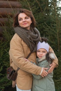 A woman and a young girl, tightly embracing outside near a Christmas tree, radiating happiness and