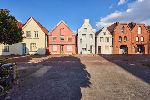 Row of houses, residential building, façade with windows, entrance doors and gables, tree, shadow,