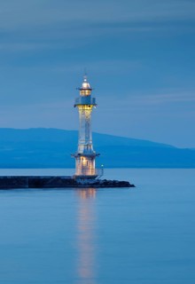Lighthouse by the harbour wall on the Lake Geneva basin at dusk, Canton Geneva, Switzerland