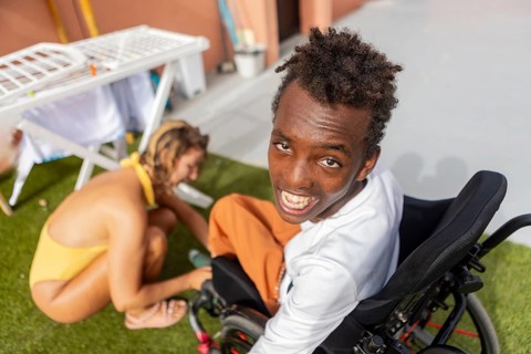 A cheerful black boy in a wheelchair with cerebral palsy in pool enjoys the sunshine as receive