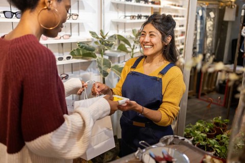 A friendly sales assistant helps a customer in a stylish sunglasses store. The woman smiles as she
