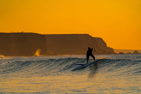 A lone surfer catches a wave as the sun sets, creating a stunning silhouette against the vibrant