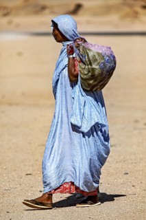 Woman in traditional dress with bag walking through a dry, sandy desert landscape, woman in the