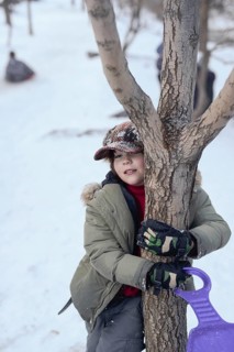 A child enjoys a snowy day at Sierra Nevada Ski Resort, Granada. Dressed warmly, they hug a tree,