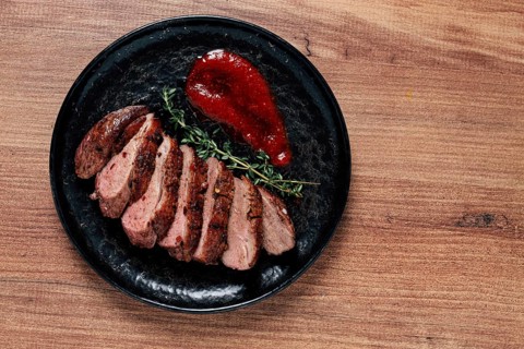 Roast duck breast, sliced on a plate, with red sauce, homemade, no people