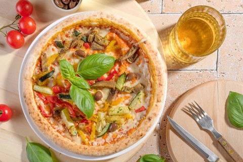 Closeup of a vegetarian pizza topped with fresh basil leaves, zucchini, eggplant, olives, and