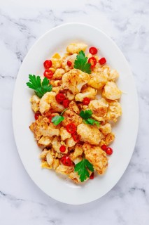 Cauliflower dish, with chili pepper and parsley, on a white plate served on a marble countertop