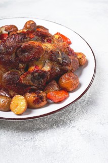 Pork knuckle baked with vegetables, new potatoes, on a white plate, homemade, no people