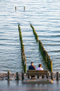An elderly couple sitting on a bench on the beach, at high tide, breakwater, Netherlands