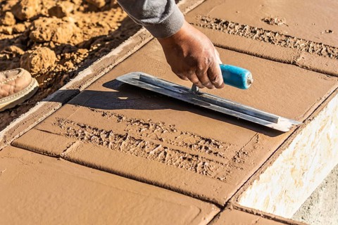 Construction Worker Using Trowel On Wet Cement Forming Coping Around New Pool