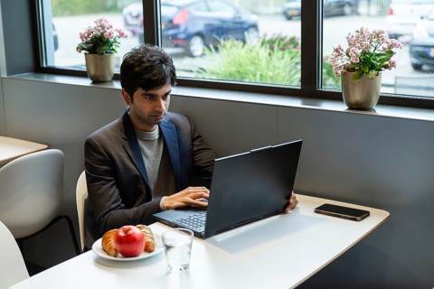 A indian man works on a laptop at a hotel cafe table in a conference of AI in Amsterdam. A