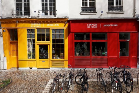 Two shop facades in yellow and red next to each other, travel agency for Latin America and for