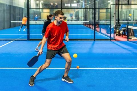 Man in motion holding a paddle on a bright blue indoor pickleball court, focusing on the yellow
