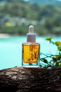 Golden cosmetic serum enriched with vitamins displayed on a tree trunk by a turquoise sea,