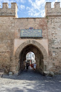 Old city gate with stone walls and a passage through which people walk, Tarifa