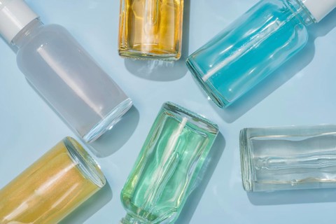 A collection of colorful glass serum bottles arranged on a light blue background. The bottles