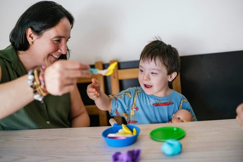 A child with Down syndrome and his mother sitting at a table engage in a creative and joyful play