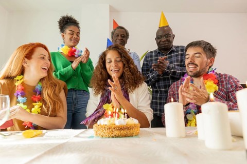 A lively birthday celebration featuring a group gathered around a cake. Party hats, colorful leis,