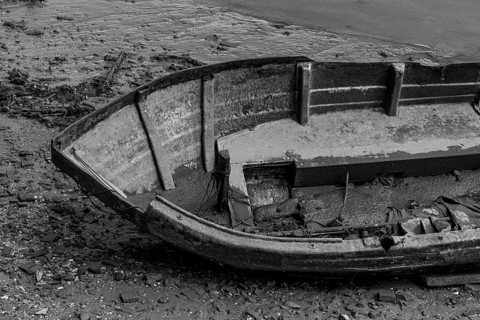 An old, abandoned boat rests silently on a muddy river shore, partially submerged, with its hull