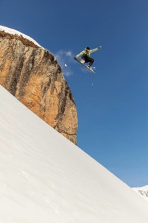 A daring snowboarder executes an exhilarating jump off a snow-covered cliff, soaring high against a