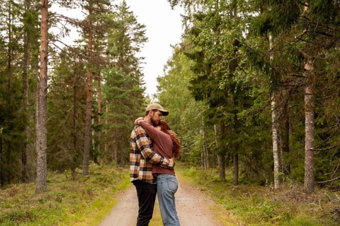 A couple embraces on a scenic path surrounded by lush green trees in a serene Swedish forest. A