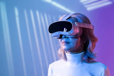 An elderly Asian woman wearing virtual reality goggles immerses herself in the metaverse. The image