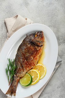 Baked dorado fish, in the oven, fried dorado, with spices and herbs, on a white plate, top view,