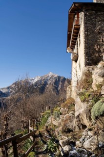 A rustic stone house with a wooden balcony, overlooking a rugged snowy mountain landscape in a