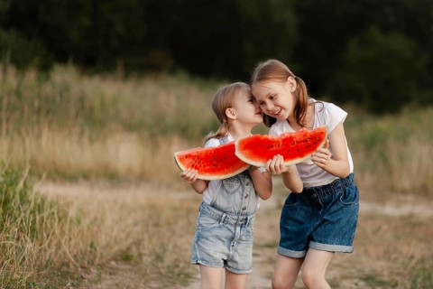 Two happy children holding slices of juicy watermelon in a sunlit field, embodying the joy and