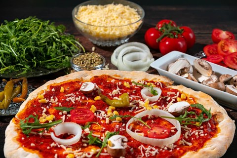 A vegetarian pizza surrounded by fresh ingredients such as tomatoes, onions and arugula